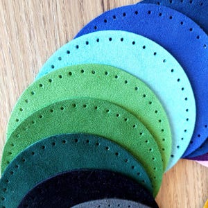 May include: A selection of circular leather bases in various shades of blue, green, and grey. Each base features evenly spaced holes around the edge, suitable for crafting. The bases are arranged in a fan, displaying the range of colours and textures.
