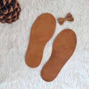 May include: Two brown leather soles with stitching around the edges and holes along the sides. A spool of brown thread is included.