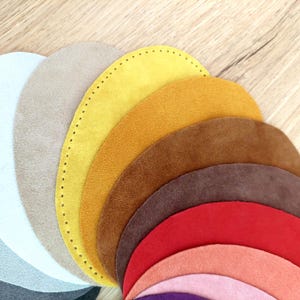 Può includere: Un set di 10 cerchi in tessuto scamosciato di vari colori, disposti a forma di arcobaleno. I cerchi sono di dimensioni diverse, con il cerchio più grande in alto e il cerchio più piccolo in basso.