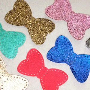 May include: A collection of colorful butterfly-shaped embellishments. The butterflies are in various colors, including gold, pink, blue, red, and teal. Each butterfly has a glittery or textured surface and is outlined with small, evenly spaced dots.
