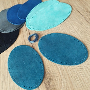 Può includere: Un assortimento di pezzi ovali in pelle scamosciata in varie tonalità di blu, verde acqua e grigio. Ogni pezzo presenta una serie di fori distanziati uniformemente lungo il bordo, per la cucitura. È presente anche un piccolo rocchetto di filo blu.