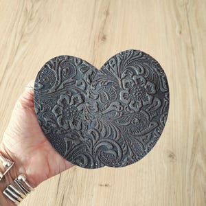 Könnte beinhalten: Zwei runde graue Lederuntersetzer mit einem geprägten Blumenmuster.