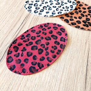 Puede incluir: Tres parches de tela ovalados con un diseño de estampado de leopardo. Los parches son de color rojo, marrón y blanco.