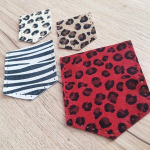 Op de afbeelding: Vier decoratieve leren zakpatches met dierenprints. Inclusief een wit-zwarte zebraprint, een rode luipaardprint en twee luipaardprintpatches in beige en crèmekleuren. Elke patch is rondom de randen gestikt.