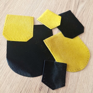 May include: A collection of yellow and black felt shapes, including rectangles and pocket-like designs, some with stitched edges. The felt has a textured finish. The pieces are arranged on a light wood surface.