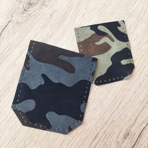 May include: Two camouflage-patterned leather pieces. One is primarily navy blue and gray, the other is olive green, brown, and black. Both have a series of small holes along the edges, suggesting they are designed to be sewn together.