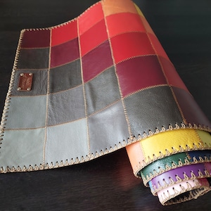 Könnte beinhalten: Ein mehrfarbiger Leder-Patchwork-Teppich mit einem genähten Rand. Der Teppich ist aufgerollt und zeigt die verschiedenen Farben des Patchworks.