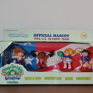 May include: A Cabbage Patch Kids Olympikids collectible set featuring four figurines representing different sports: track and field, weightlifting, tennis, and gymnastics. The figurines are dressed in red, white, and blue, and the box features the 1996 U.S. Olympic Team logo.