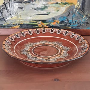 Peut inclure: Une grande assiette ronde en céramique brune avec une bordure décorative blanche et bleue. L'assiette a un centre surélevé avec un motif circulaire plus petit.