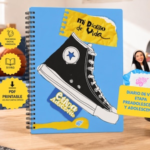 Könnte beinhalten: Ein hellblaues Notizbuch mit Spiralbindung, das eine Illustration eines schwarzen High-Top-Sneakers, eine gelbe Grafik aus zerrissenem Papier mit dem Text 'mi Diario de Vida' und einen blauen Aufkleber mit dem Text 'Etapa Adolescente' zeigt.