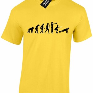 May include: Yellow t-shirt featuring a black silhouette of the evolution of man, culminating in a man performing a kettlebell squat and a man doing a push-up.