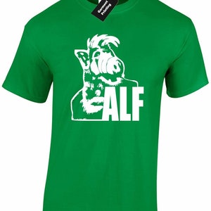 May include: A vibrant green t-shirt with a white graphic of the character ALF and the name "ALF" in white block letters. The shirt has a crew neck and short sleeves. A black tag with white text is attached to the collar.
