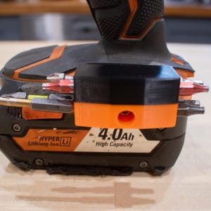 May include: Close-up of a black and orange power drill with a black bit holder attached. The drill has a 4.0Ah high capacity battery. The bit holder is orange and black and holds several drill bits.