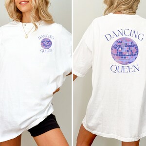 Könnte beinhalten: Weißes Oversize-T-Shirt mit einem lilafarbenen Discokugel-Motiv und dem Text "Dancing Queen" auf der Vorder- und Rückseite.