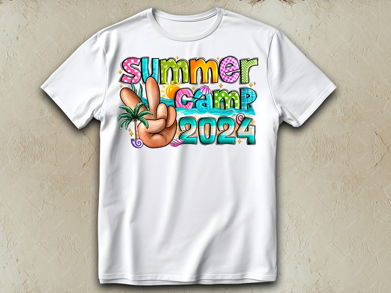 May include: White t-shirt featuring a colourful graphic design that reads "Summer Camp 2024". The design includes a peace sign, a palm tree, and seashells.