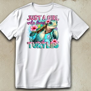 May include: White t-shirt featuring a colorful graphic of a sea turtle with pink flowers and the text "JUST A GIRL who loves TURTLES". The design includes blue and turquoise accents.