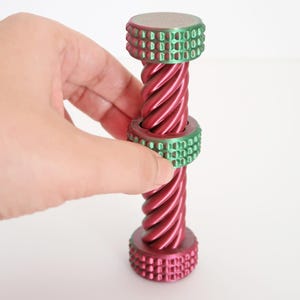 Peut inclure: Un bouchon de bouteille rouge et vert métallisé avec un design torsadé. Le bouchon a une forme cylindrique avec un dessus et un dessous texturés, et une bande verte au milieu. Le bouchon est tenu sur un fond blanc.