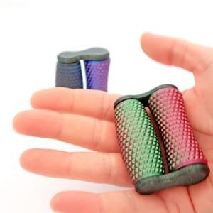 Peut inclure: Une main tient deux paires d'objets cylindriques colorés et texturés. Une paire est verte et rouge, l'autre est bleue et violette. Les objets ont un motif en losange et une pièce de connexion gris foncé.