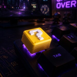 Può includere: Un tasto meccanico quadrato di colore giallo con un punto interrogativo bianco. Il tasto è illuminato dal basso con una luce viola ed è posizionato su una tastiera nera accanto al tasto tab, con una postazione da gioco sullo sfondo.