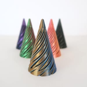 Può includere: Una collezione di sei oggetti decorativi a forma di cono in vari colori, tra cui viola, verde, oro, corallo e nero. Ogni cono presenta un design a spirale con una lucentezza metallica, su sfondo bianco.
