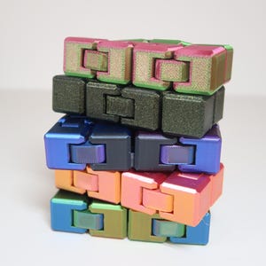 Può includere: Una pila di giocattoli fidget colorati nelle tonalità di blu, verde, rosa e arancione. Ogni pezzo a forma di cubo è collegato, consentendo un movimento flessibile. I giocattoli hanno una lucentezza metallica, creando un display visivamente accattivante.