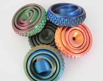 May include: A selection of metallic fidget spinners in green, blue, and orange. Each spinner has a unique design, with textured edges and concentric circles. The spinners are arranged on a white background. Measurements are in cm.