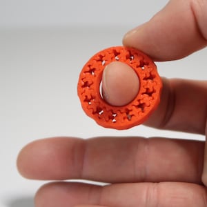 Peut inclure: Un objet circulaire orange vif avec un motif ajouré détaillé. L'objet est tenu entre les doigts, mettant en valeur son design complexe. Le motif est un motif floral ou étoilé répétitif, créant un élément décoratif.