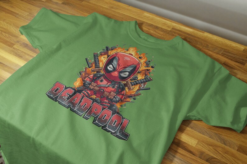 Puede incluir: Camiseta verde con una imagen de dibujos animados de Deadpool con un traje rojo y negro, rodeado de llamas y armas. El texto "DEADPOOL" est&aacute; impreso en blanco y negro debajo de la imagen.