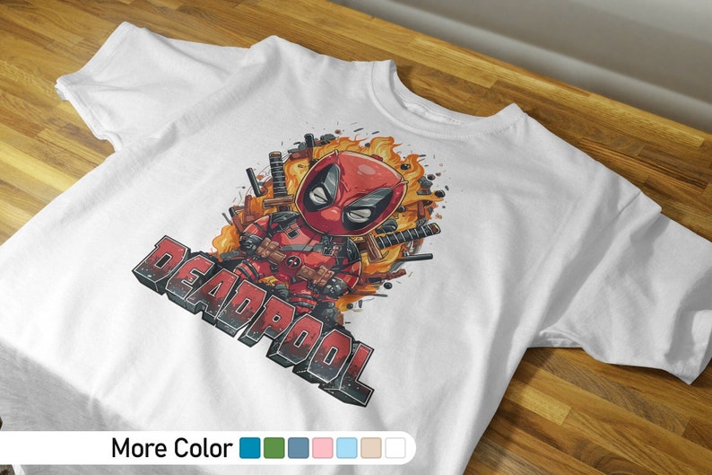 Puede incluir: Camiseta blanca con una imagen de dibujos animados de Deadpool con un traje rojo y negro, sosteniendo una espada. La imagen est&aacute; rodeada de llamas y la palabra "DEADPOOL" est&aacute; escrita en letras negras y rojas.