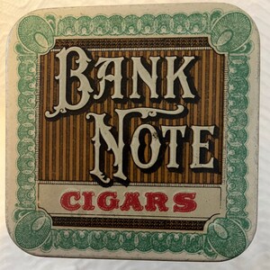 May include: A vintage tin box with a green and white border design. The box features the text "Bank Note Cigars" in a decorative font.