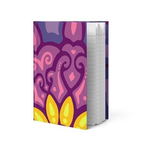 May include: A hardcover notebook with a vibrant, abstract floral design. The cover features a pattern of purple, pink, and yellow shapes. The notebook's pages are lined and visible on the right side.