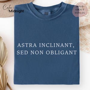 May include: A midnight blue crew neck t-shirt featuring the white text ASTRA INCLINANT, SED NON OBLIGANT printed across the chest. The shirt has a Comfort Colors label at the inner neckline and a short-sleeved, casual design.