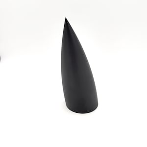 May include: A solid black, elongated cone-shaped object with a smooth, matte finish. The object features a wide, circular base that tapers gradually to a sharp, pointed tip, standing upright against a plain, neutral white background.