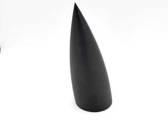Könnte beinhalten: Ein massives, schwarzes, längliches, kegelförmiges Objekt mit einer glatten, matten Oberfläche. Das Objekt hat eine breite, kreisförmige Basis, die sich allmählich zu einer scharfen Spitze verjüngt und auf einem neutralen weißen Hintergrund steht.
