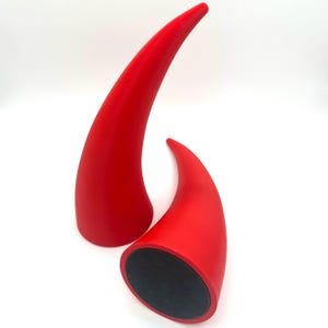 May include: Two red horns, one larger than the other, are made of a smooth, solid material. The horns are curved and pointed at the tip. The base of the horns is black.