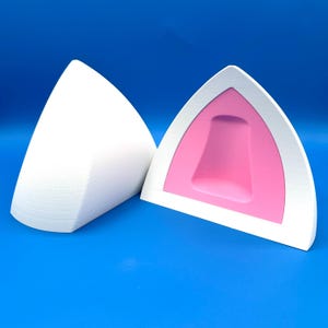 K&ouml;nnte beinhalten: Zwei wei&szlig;e Katzenohren-Accessoires mit rosa Innenraum und wei&szlig;em Rand. Ein Ohr ist durchgehend wei&szlig;, w&auml;hrend das andere das rosa Innenohr zeigt. Die Artikel sind vor einem hellblauen Hintergrund platziert.