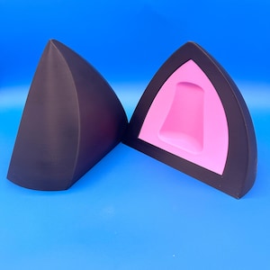 K&ouml;nnte beinhalten: Zwei schwarze Katzenohren-Accessoires, eines massiv und das andere aufgeschnitten, um ein rosa Innenleben zu zeigen. Die Ohren heben sich vor einem leuchtend blauen Hintergrund ab und erzeugen einen auff&auml;lligen Kontrast. Das Design ist schlicht und modern.