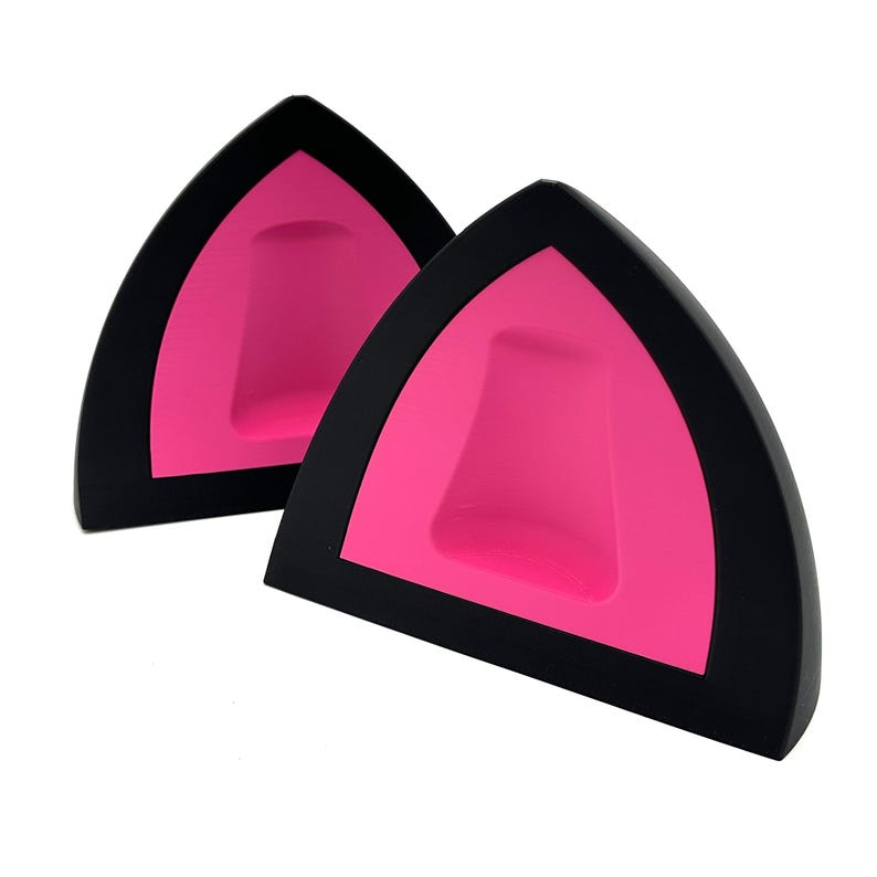 K&ouml;nnte beinhalten: Zwei schwarze Katzenohrzubeh&ouml;rteile mit leuchtend rosa Innenr&auml;umen. Die Ohren sind dreieckig und haben eine glatte, matte Oberfl&auml;che. Die Accessoires sind zum Tragen auf dem Kopf bestimmt, wahrscheinlich als Teil eines Kost&uuml;ms oder f&uuml;r Cosplay.