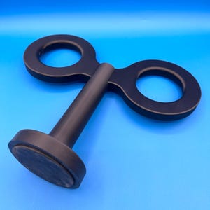 May include: A black, double-ended bottle stopper with a circular handle on each end and a cylindrical stem. The stopper has a flat, circular base. The object is set against a bright blue background.