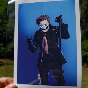 Könnte beinhalten: Illustration eines Künstlers in schwarzem Anzug, weißer Maske und Handschuhen, der ein Mikrofon hält. Das Kunstwerk zeigt einen blauen Hintergrund und einen rosa-weißen Schal. Die Signatur des Künstlers, GreenFa99, ist unten rechts sichtbar.