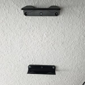 May include: Two black metal wall mounts with screws. The mounts are designed to hold a shelf or other object.