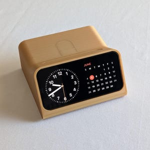 Può includere: Un supporto in legno beige con un iPhone nero che mostra un orologio e un calendario. Il calendario mostra il mese di giugno con il 5 evidenziato.