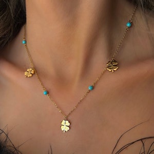 Puede incluir: Collar dorado con dijes de trébol de cuatro hojas y cuentas turquesas. La delicada cadena está adornada con múltiples colgantes de trébol y pequeños detalles turquesas, creando un accesorio elegante. El collar está diseñado para ser usado alrededor del cuello.