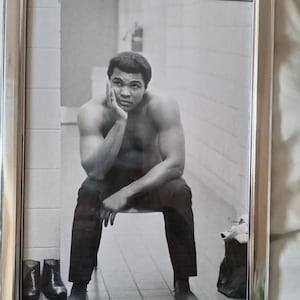 Può includere: Fotografia in bianco e nero incorniciata di un uomo seduto, che appoggia la testa sulla mano. È a torso nudo, indossa pantaloni scuri ed è seduto su una sedia. Gli stivali sono visibili sul pavimento. La fotografia è in una cornice argentata.