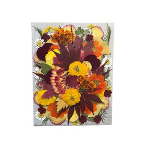 May include: A pressed flower artwork featuring a selection of dried flowers and leaves in shades of yellow, orange, red, and burgundy. The flowers are arranged in a bouquet-like shape on a canvas background.