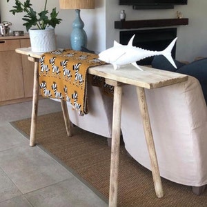 May include: A wooden console table with a zebra patterned throw blanket and a white ceramic fish sculpture on top. The table has a natural wood finish and is supported by four legs.