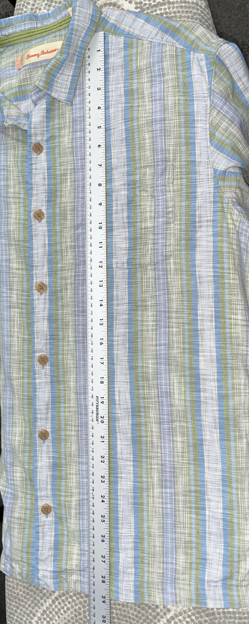 May include: A button-down shirt with vertical stripes in blue, green, and white. The shirt has a chest pocket and wooden buttons. The shirt measures approximately 30 inches in length.