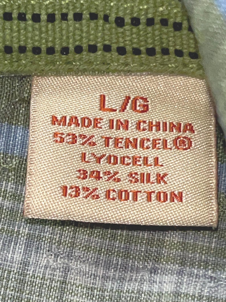 May include: Close-up of a clothing label with the text "L/G MADE IN CHINA 53% TENCEL&reg; LYOCELL 34% SILK 13% COTTON". The label is rectangular and beige, set against a green and blue patterned fabric.