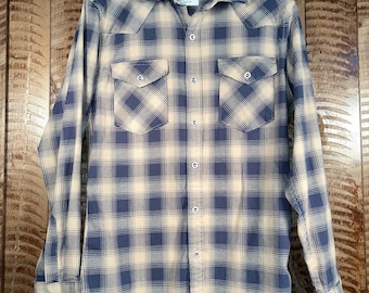 May include: A blue and tan plaid long-sleeved button-up shirt with a Wrangler label. The shirt has two chest pockets with button closures.