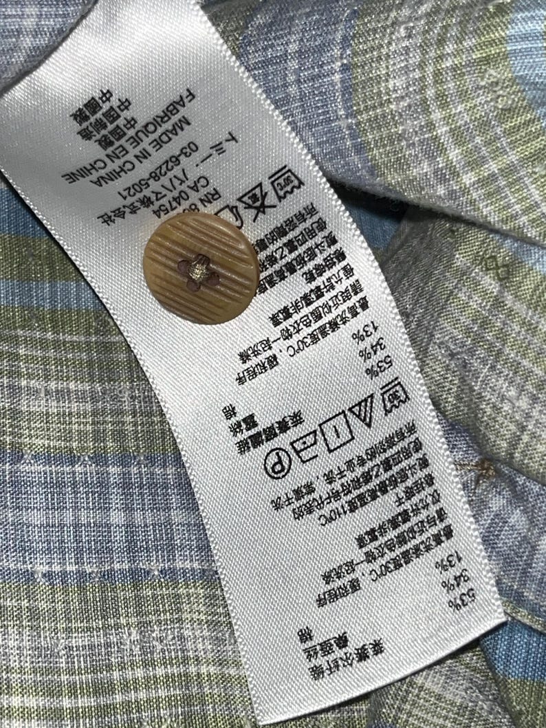 May include: Close-up of a fabric tag with a brown button. The tag includes text in multiple languages, care instructions, and fabric composition percentages: 53% Lyocell, 34% Silk, and 13% Cotton. The tag reads "Made in China".